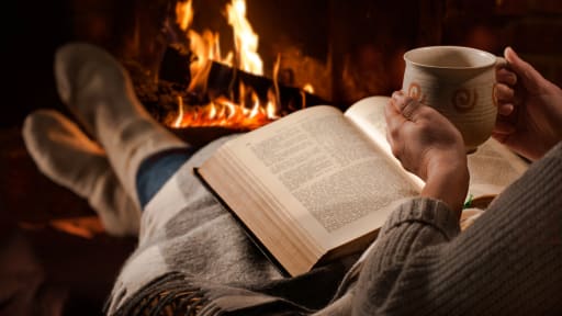 Eine Frau liest ein Buch an einem Kaminfeuer