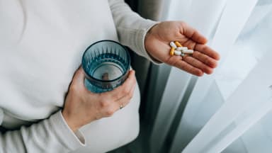 pregnant woman holding pills and glass of water in hands
