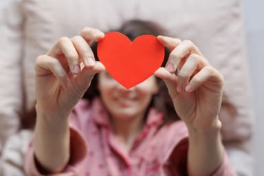 Person in einem Bett hält herzförmige Postkarte