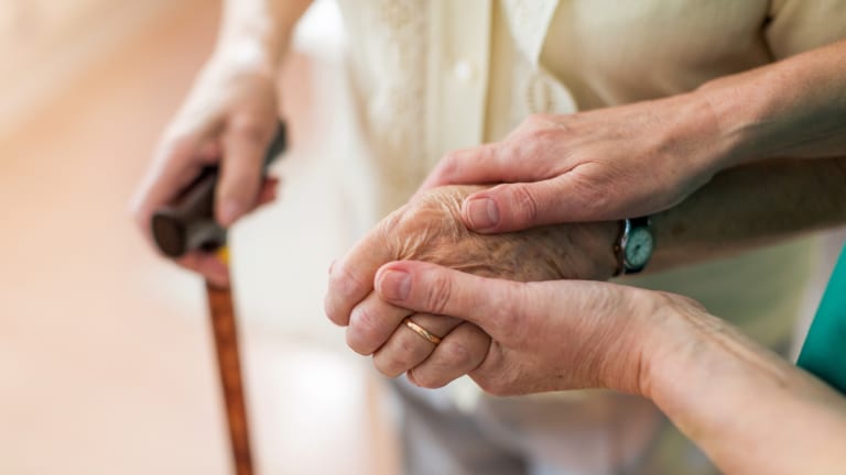Gebrechlicher Mensch wird durch jüngere Person gestützt