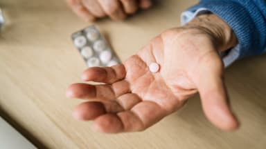 Ältere Person hält eine Pille in der Hand