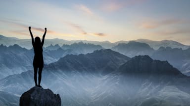 Frau steht mit erhobenen Armen auf einem Berggipfel