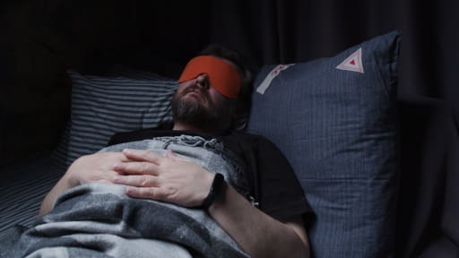 Mann liegt mit Schlafmaske in einem dunklen Zimmer