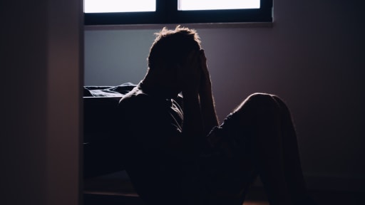 Silhouette eines Mannes, der auf dem Boden eines abgedunkelten Schlafzimmers sitzt