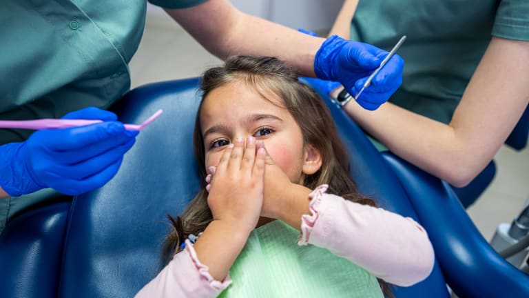 Kind hält sich bei einer zahnärztlichen Untersuchung die Hände vor den Mund