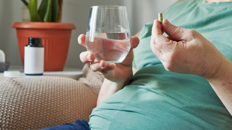 Ältere Frau hält eine Tablette und ein Glas Wasser in den Händen